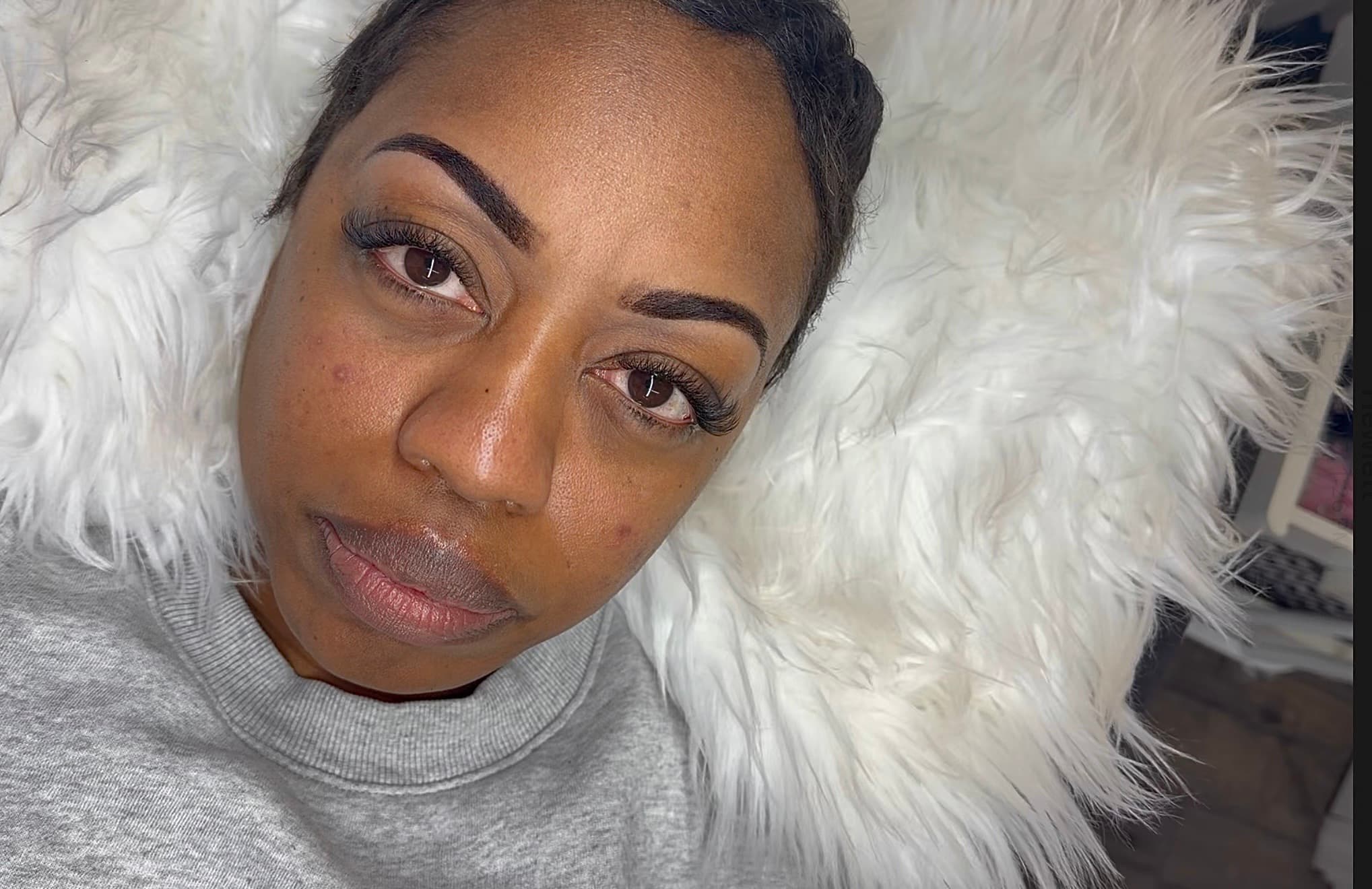 Black woman with defined eyebrows and eyelash extensions resting on a white fluffy rug.