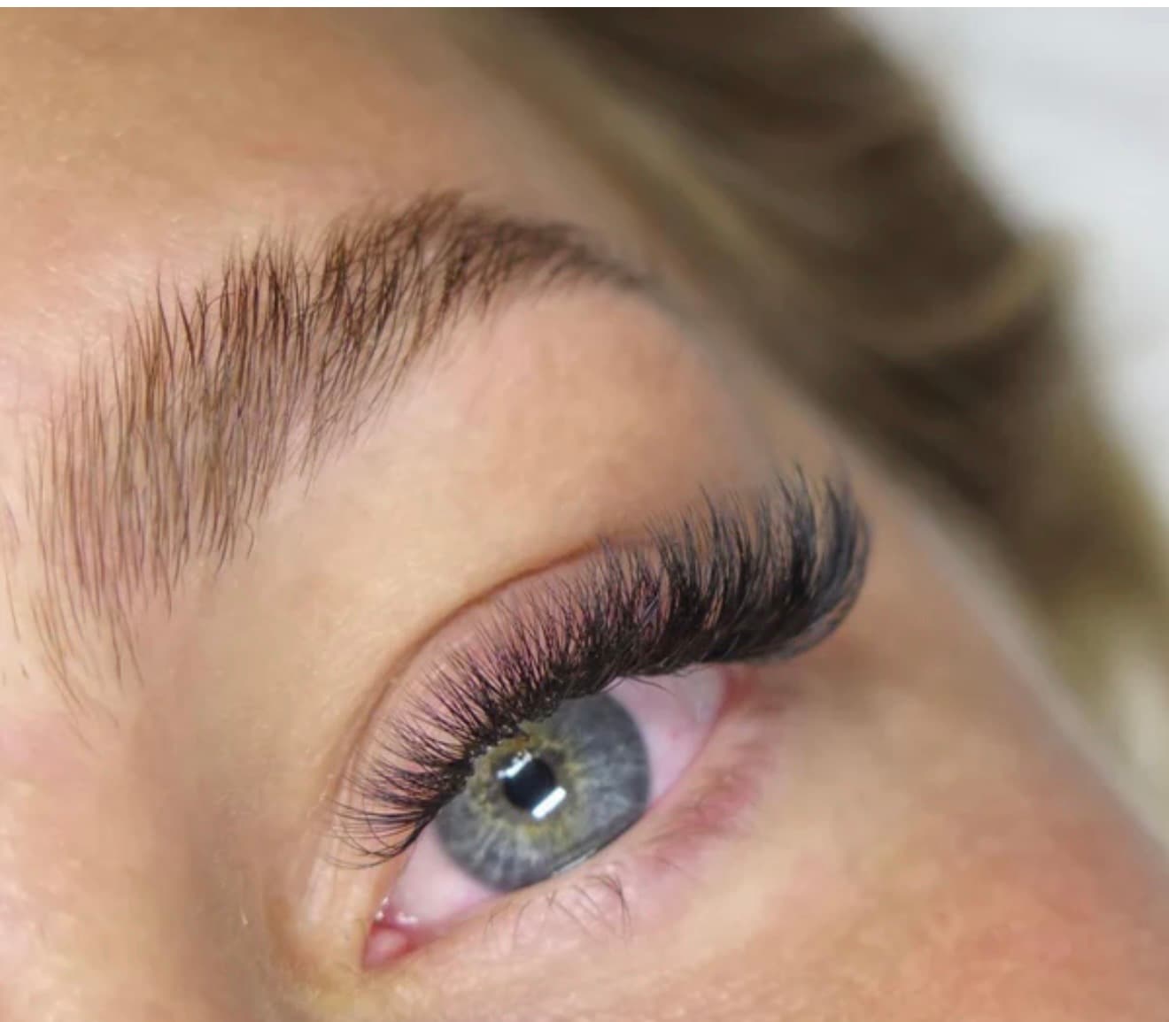 Close-up of a blue eye with full black eyelash extensions and a groomed brown eyebrow.