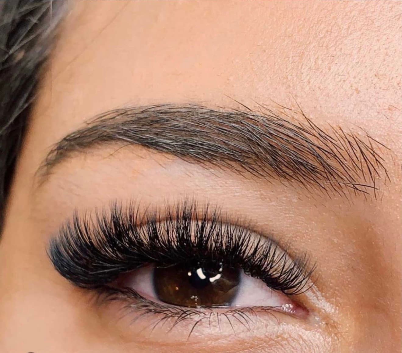 Close-up of a brown eye with thick, voluminous black eyelash extensions and groomed eyebrow.